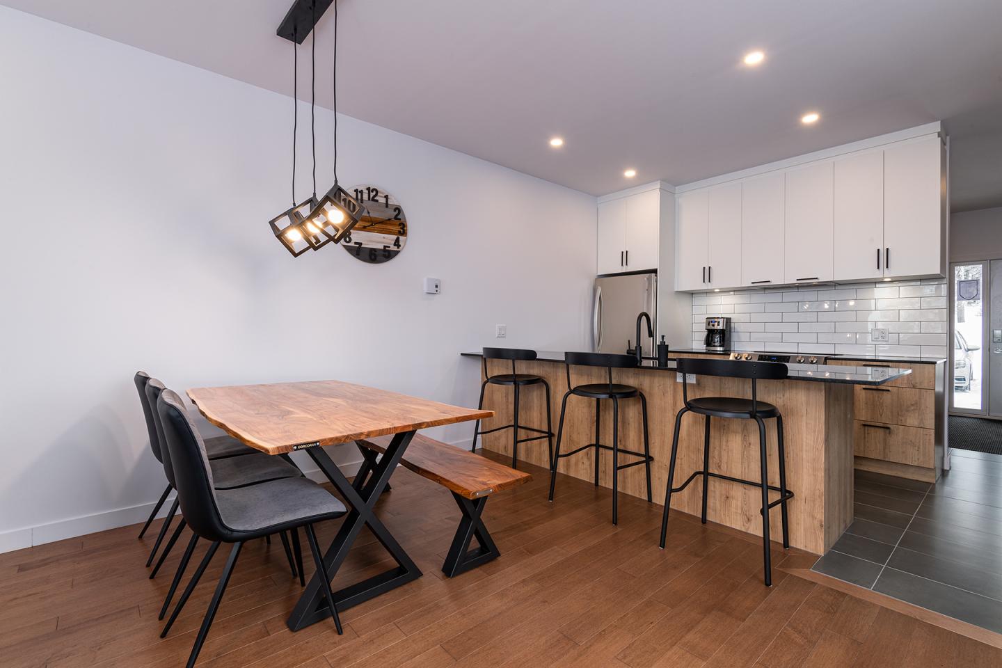Salle à manger moderne avec table en bois, quatre chaises et cuisine ouverte.