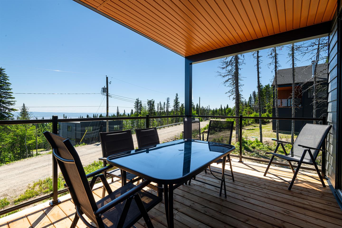 Terrasse en bois avec table, chaises, vue sur arbres et ciel bleu.