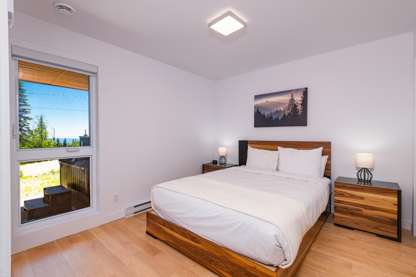 Chambre moderne avec lit double, fenêtre lumineuse et vue sur la nature.