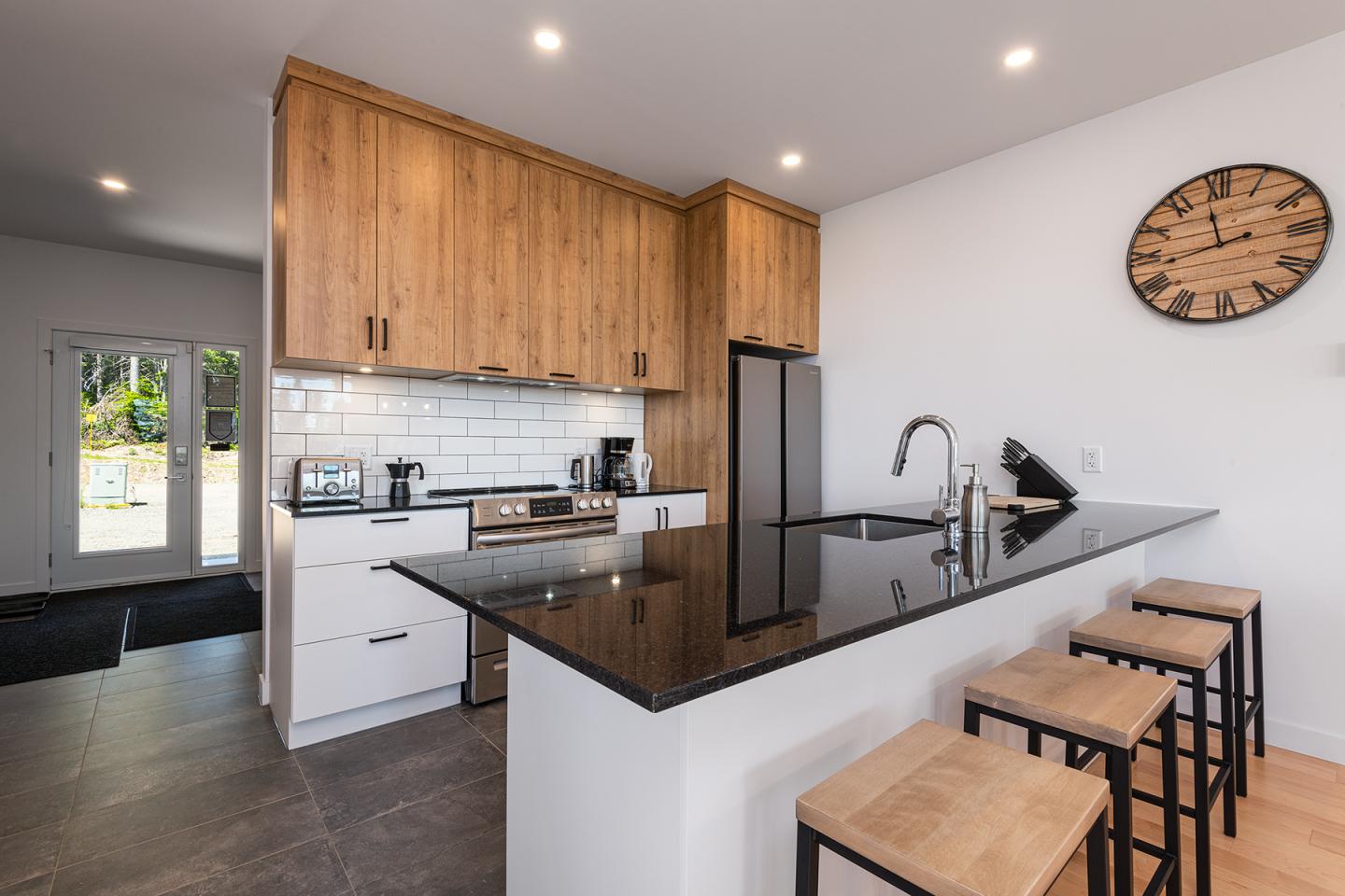 Cuisine moderne avec îlot, chaises hautes, comptoir noir, et horloge murale.