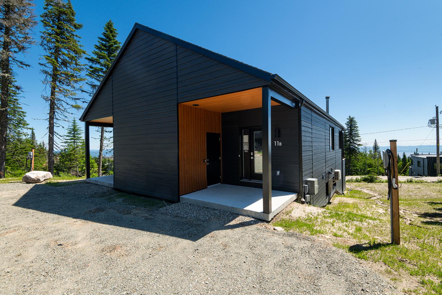 Maison moderne noire en bois, entourée d'arbres, sous un ciel bleu.