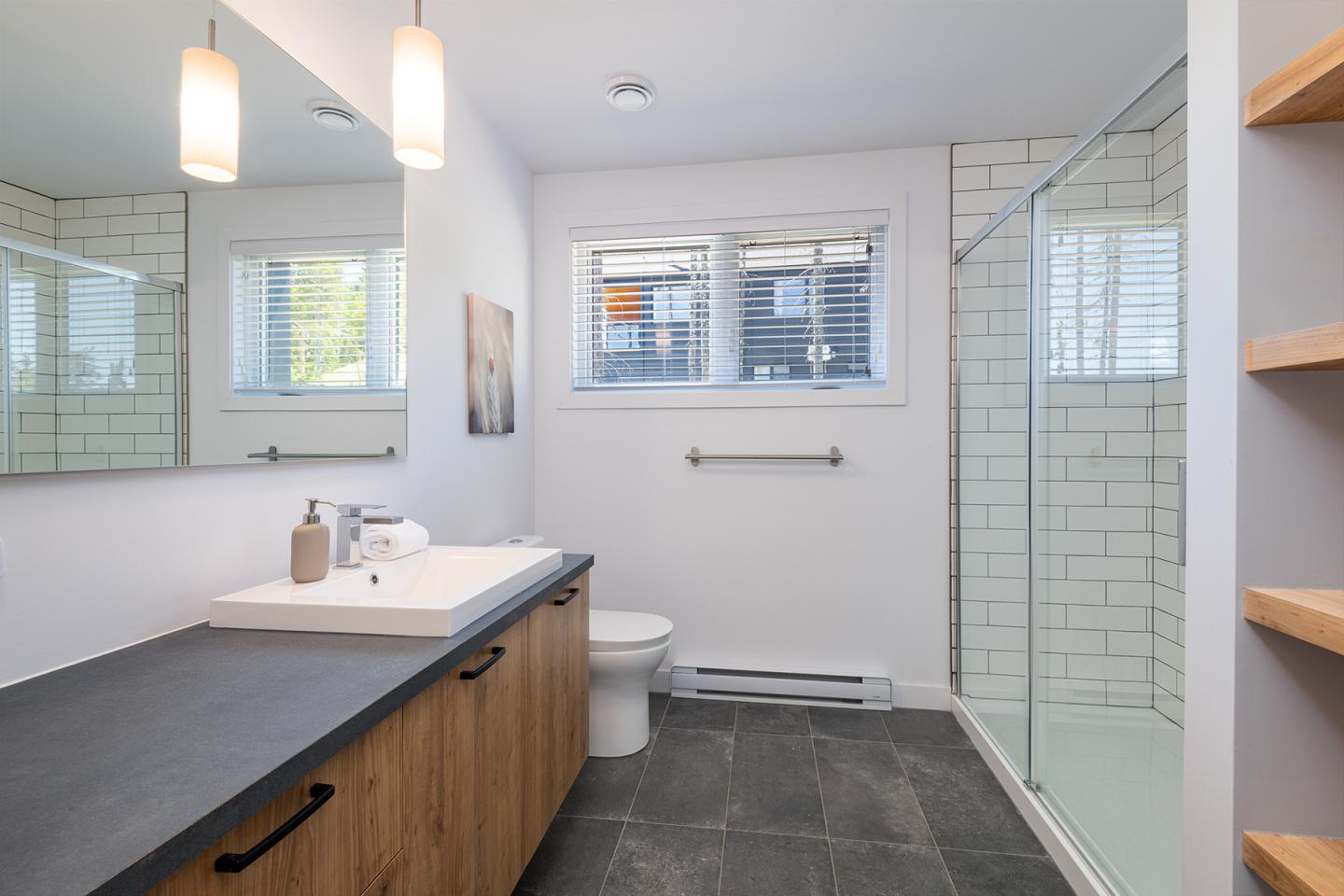 Salle de bain moderne avec douche vitrée, lavabo et lumière naturelle.