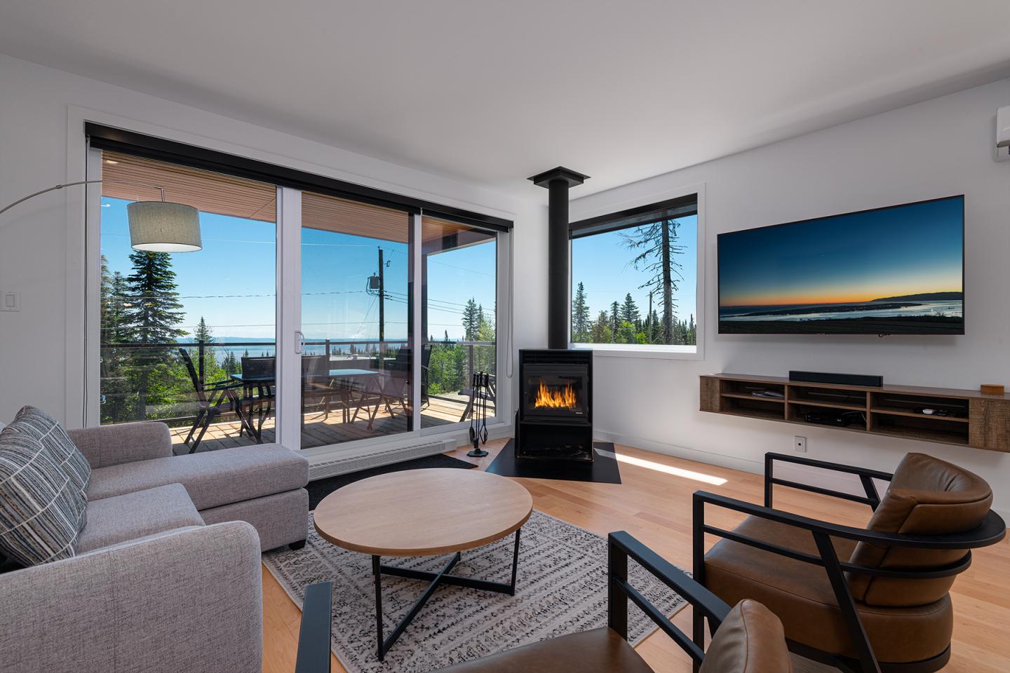 Salon moderne avec cheminée, vue sur terrasse et écran mural, décor chaleureux.