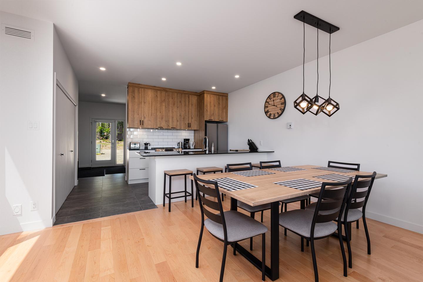 Salle à manger moderne avec table en bois, cuisine ouverte et luminaire suspendu.