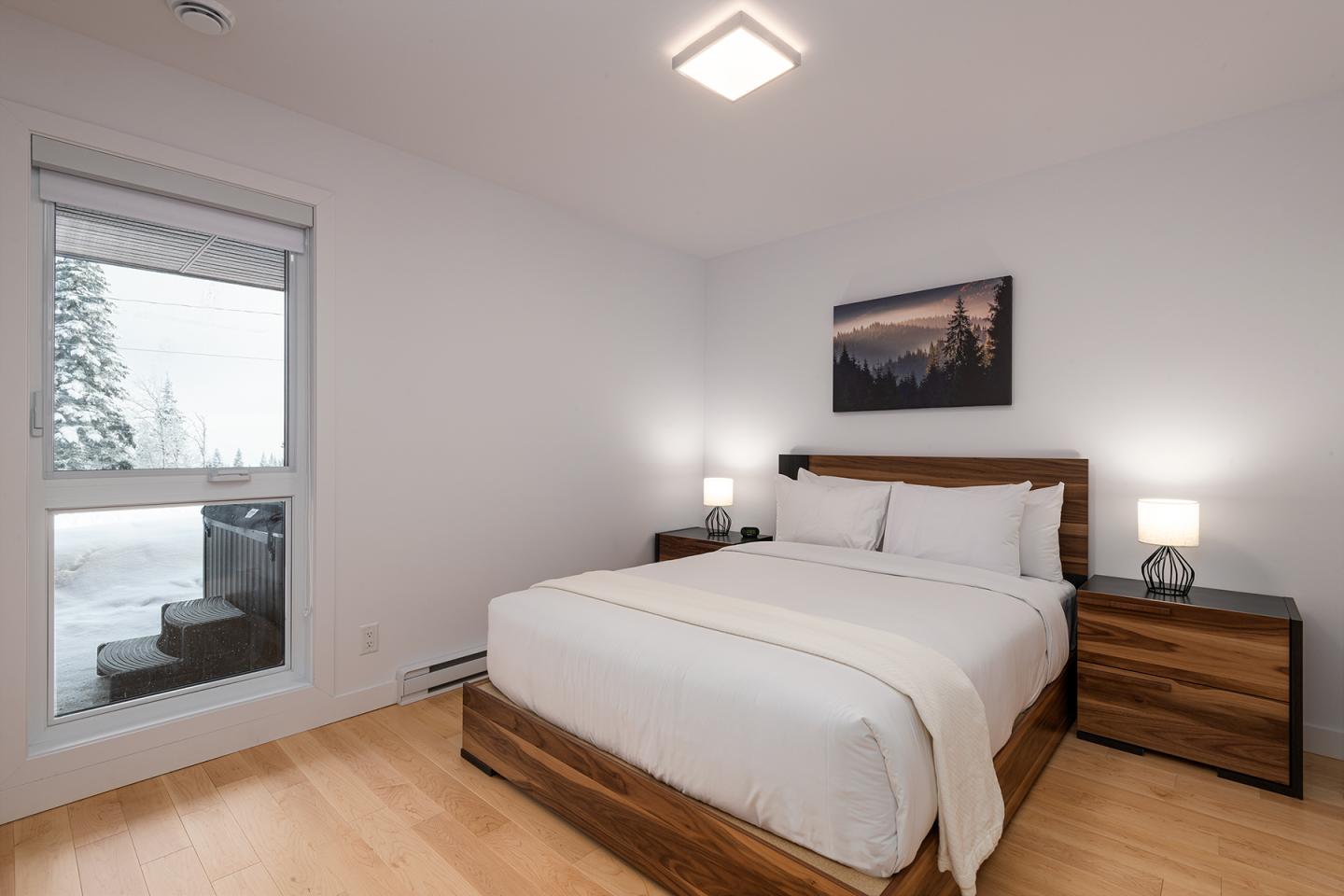 Chambre moderne avec lit double, tables de chevet et fenêtre donnant sur la neige.