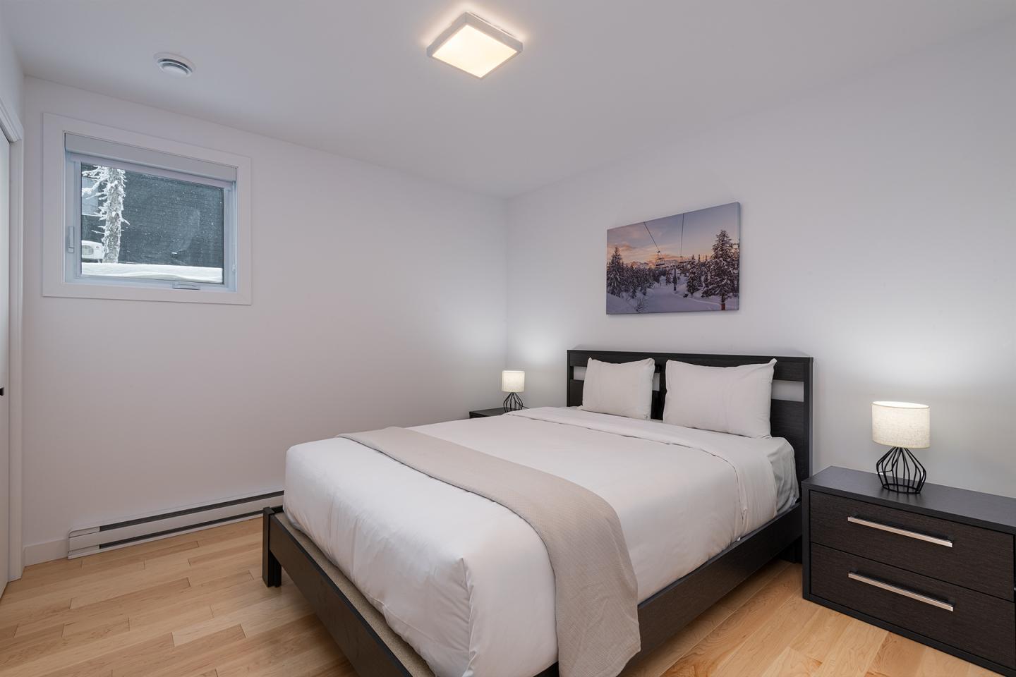 Chambre moderne, lit double avec draps blancs, deux tables de chevet et une lampe.