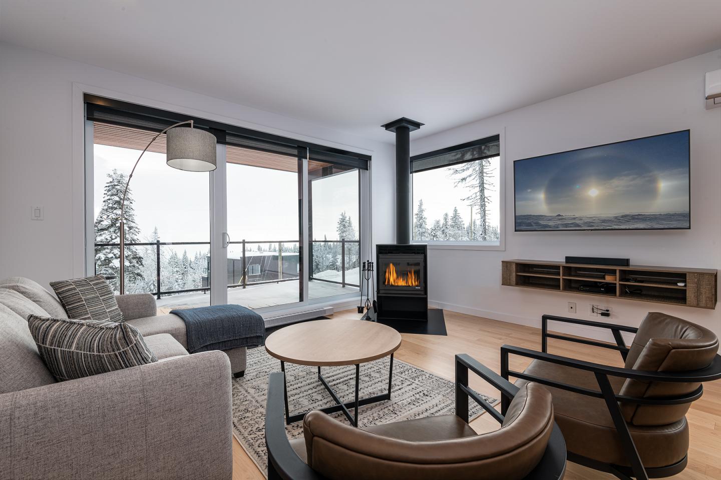 Salon moderne avec cheminée, grandes fenêtres et vue sur la neige.