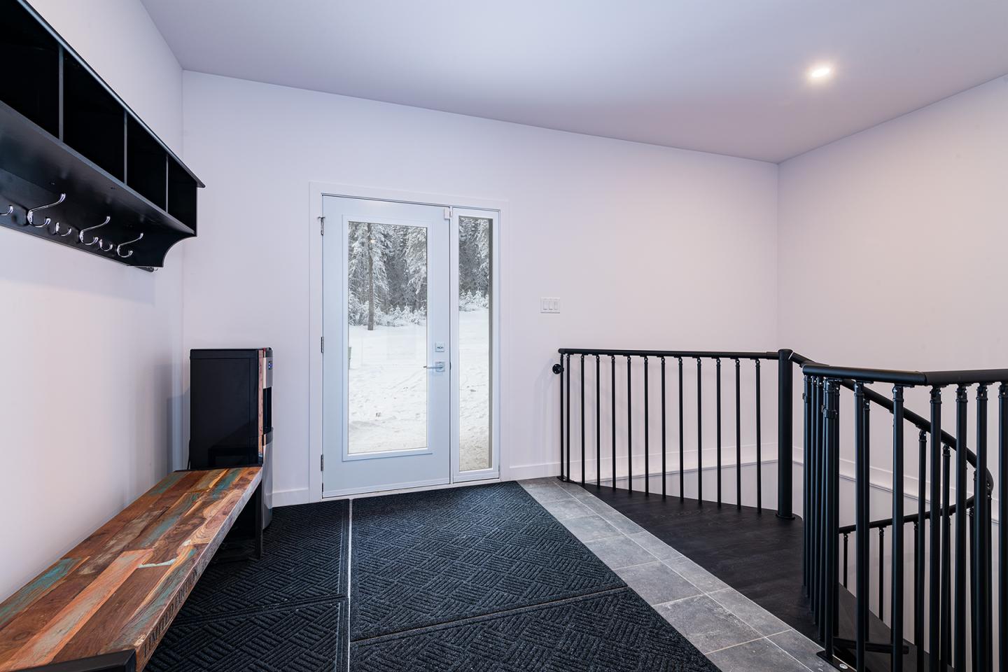 Couloir moderne avec banc en bois, rambarde noire et porte-fenêtre donnant sur la neige.