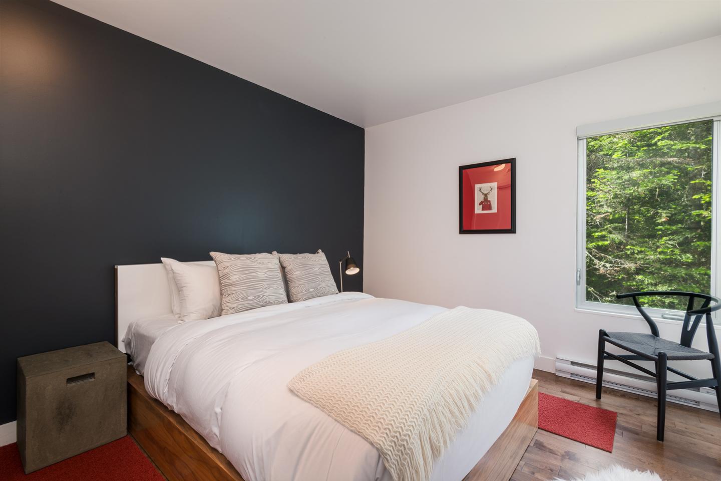 Chambre moderne avec lit double, mur noir, et fenêtre donnant sur des arbres verts.