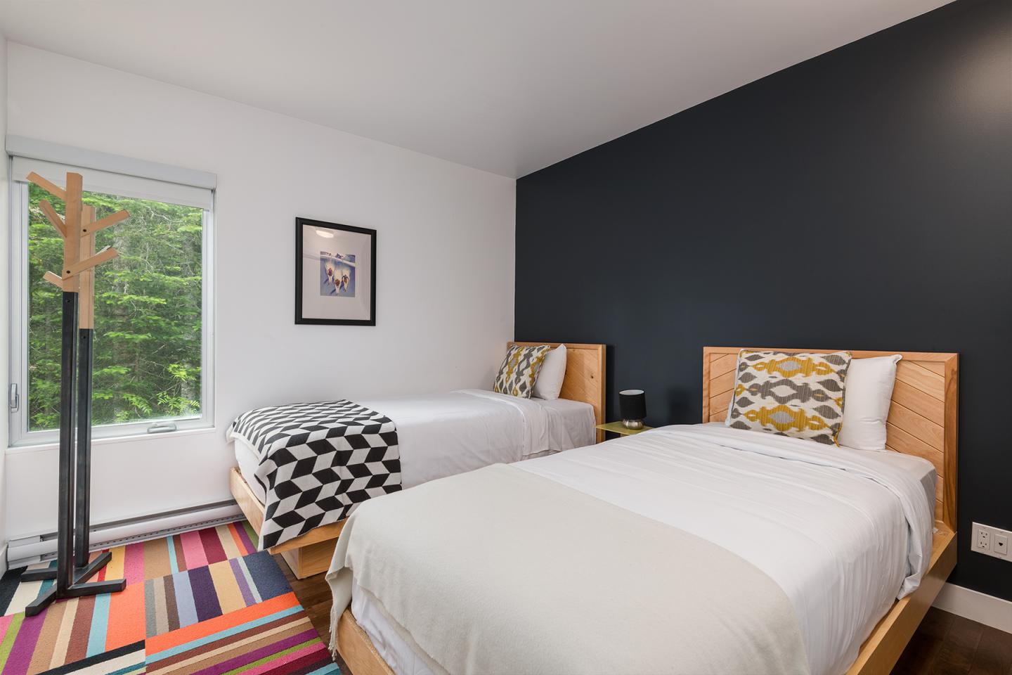 Deux lits jumeaux dans une chambre moderne avec mur noir et sol coloré.