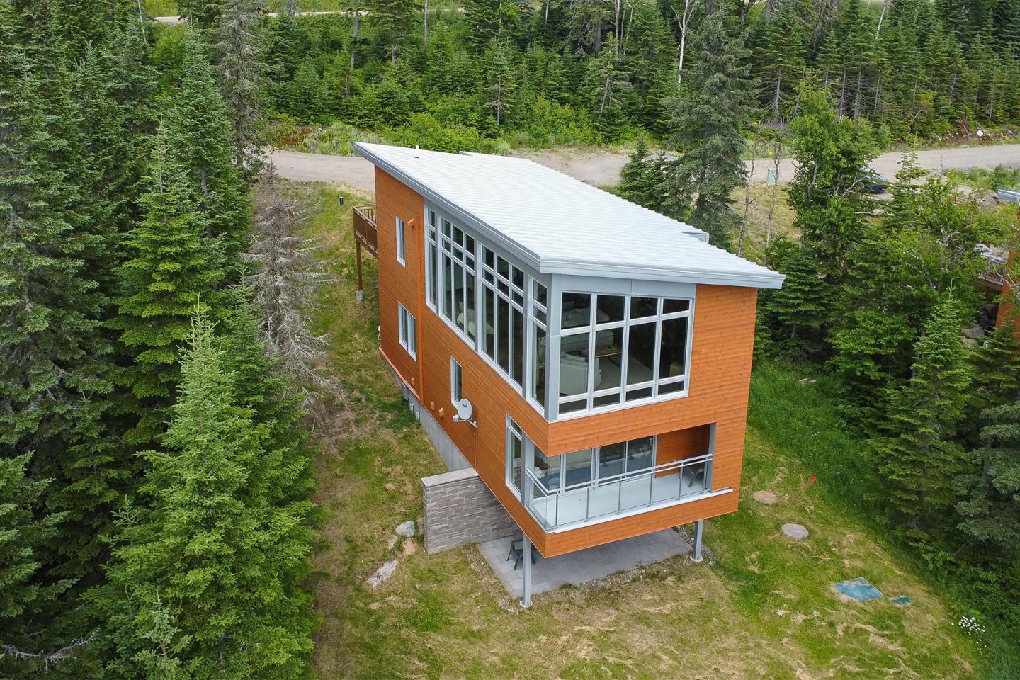 Maison moderne en briques orange avec toit blanc, entourée de pins verts.