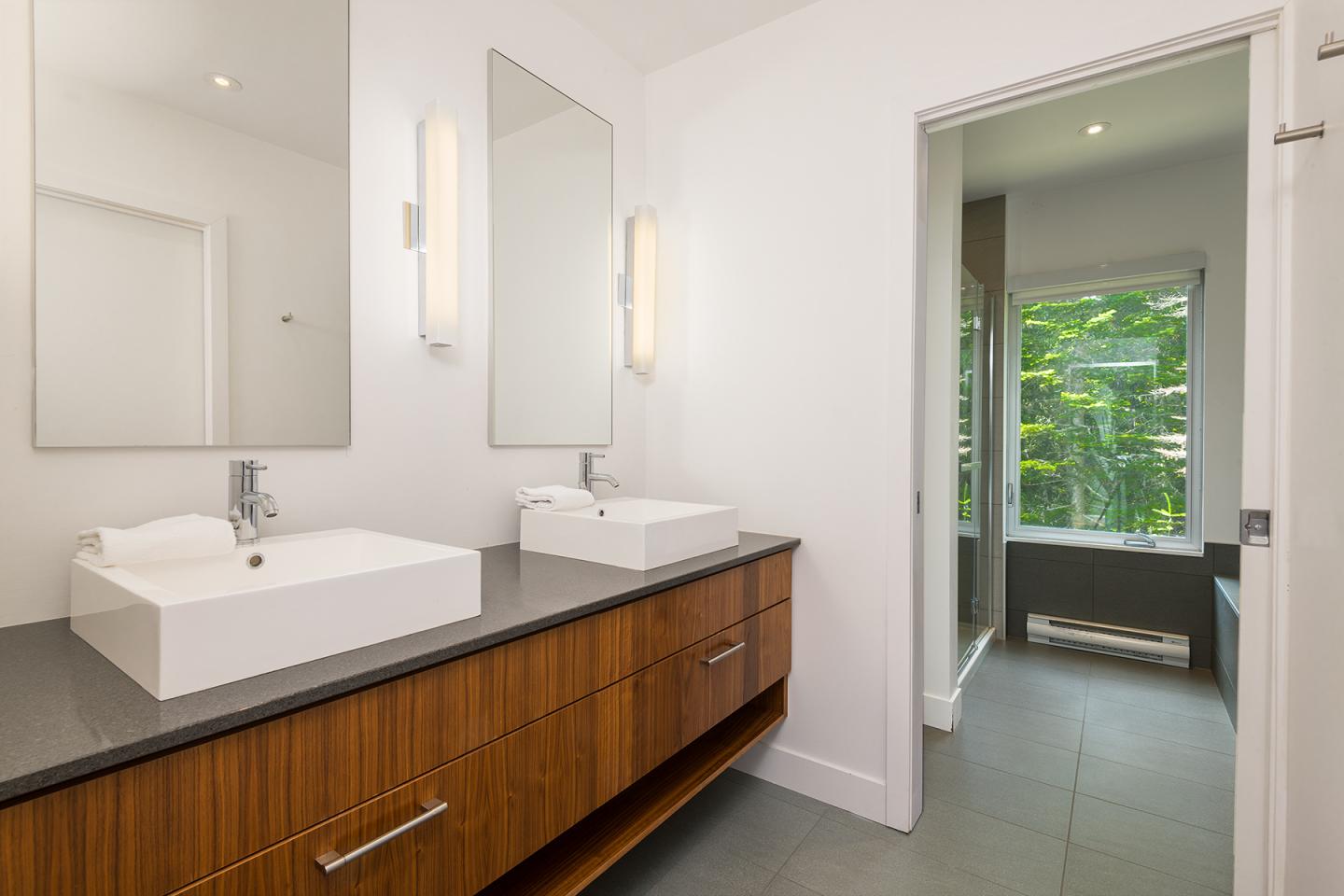 Salle de bain moderne avec deux lavabos sur un meuble en bois. Fenêtre montrant la verdure.