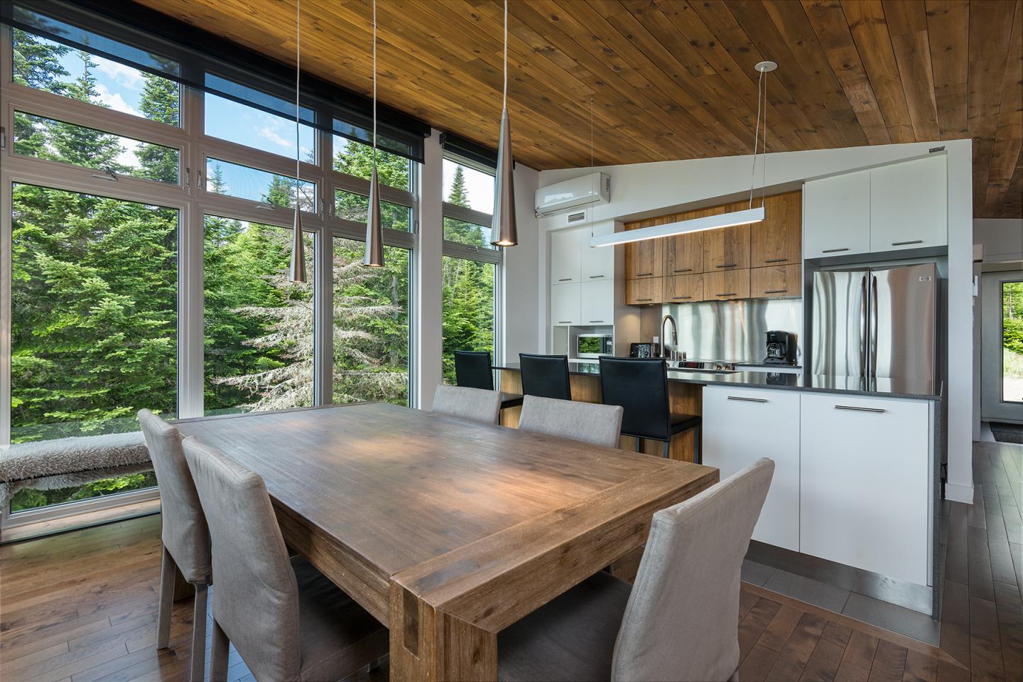 Salle à manger moderne avec table en bois, grandes fenêtres donnant sur la forêt.