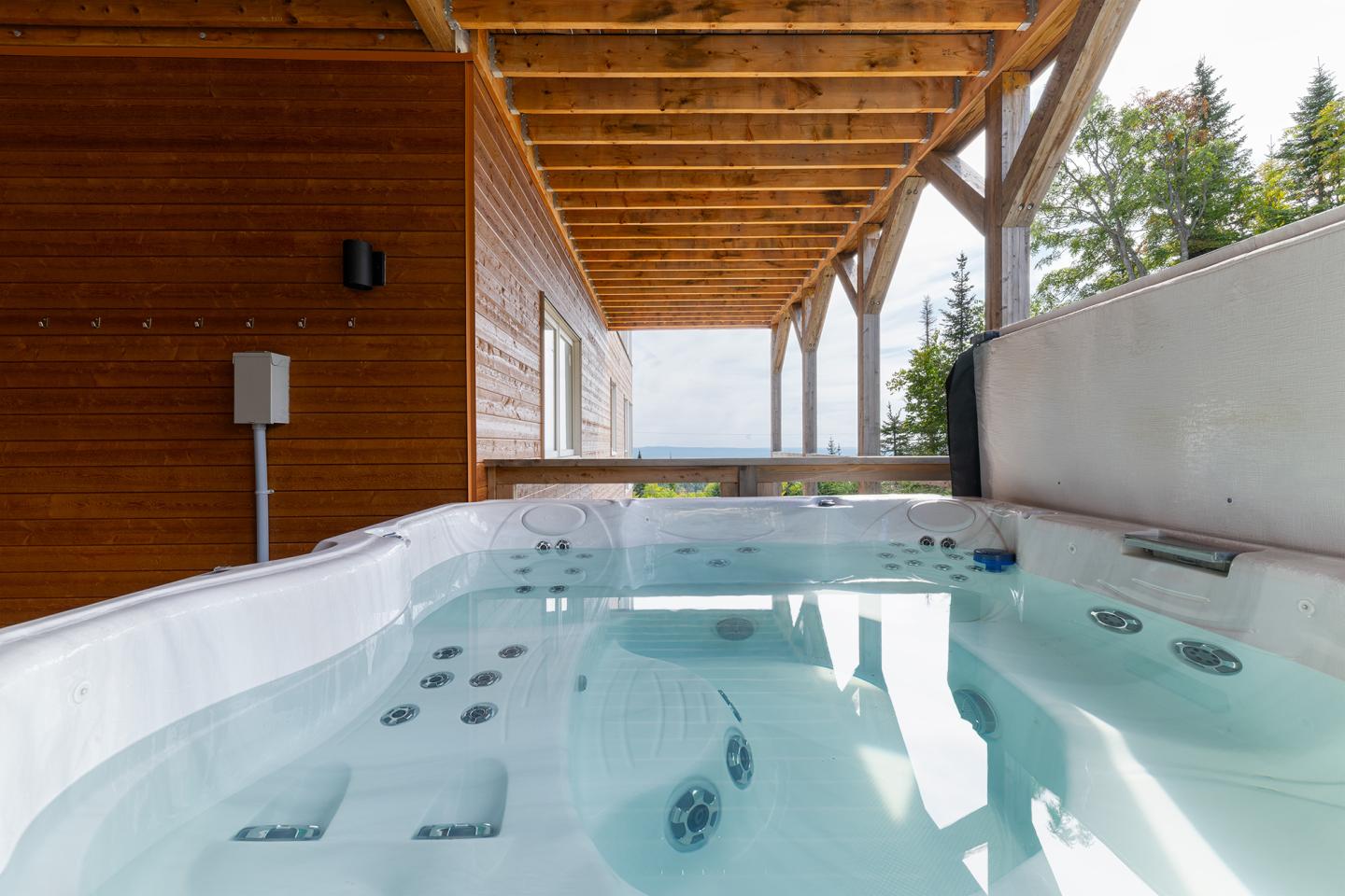 Jacuzzi sur terrasse en bois, vue sur forêt et ciel bleu.