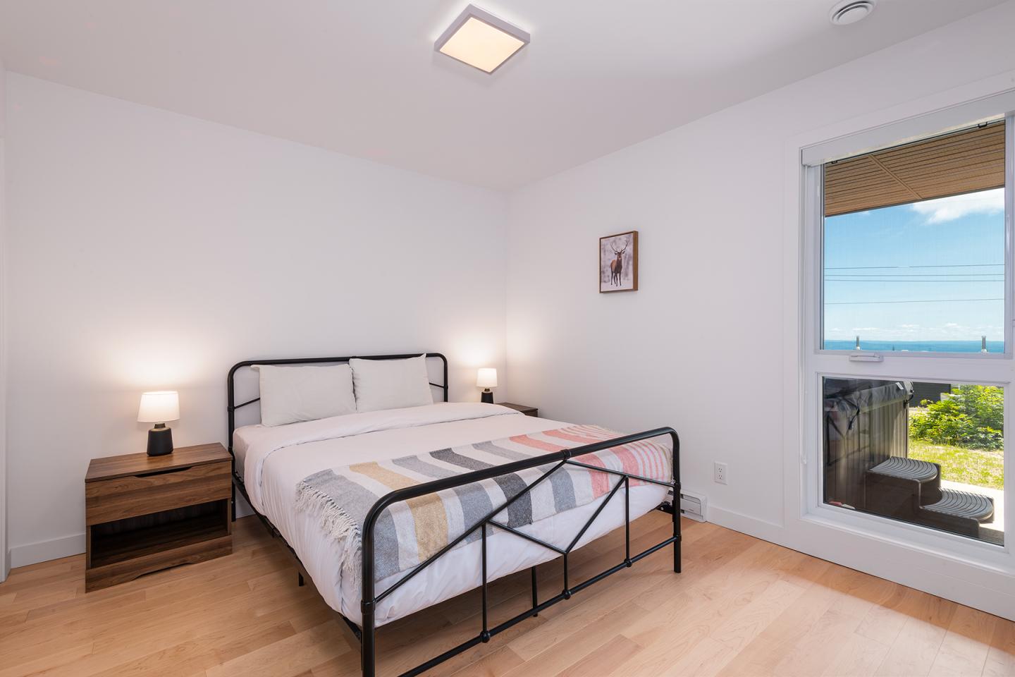 Chambre moderne avec lit double, lampe sur table de nuit, fenêtre ouverte sur le jardin.