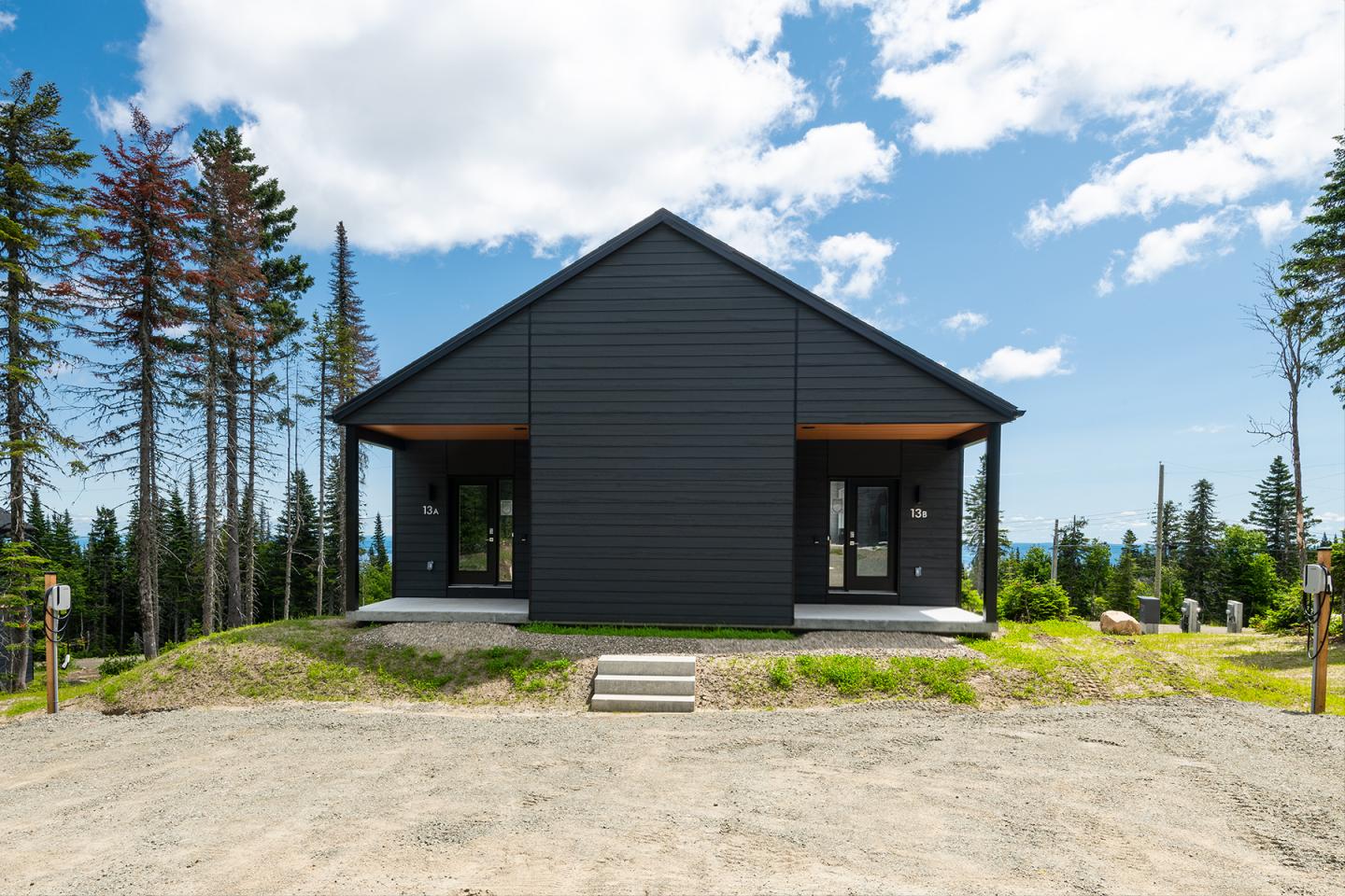 Maison moderne noire, entourée d'arbres sous un ciel bleu.