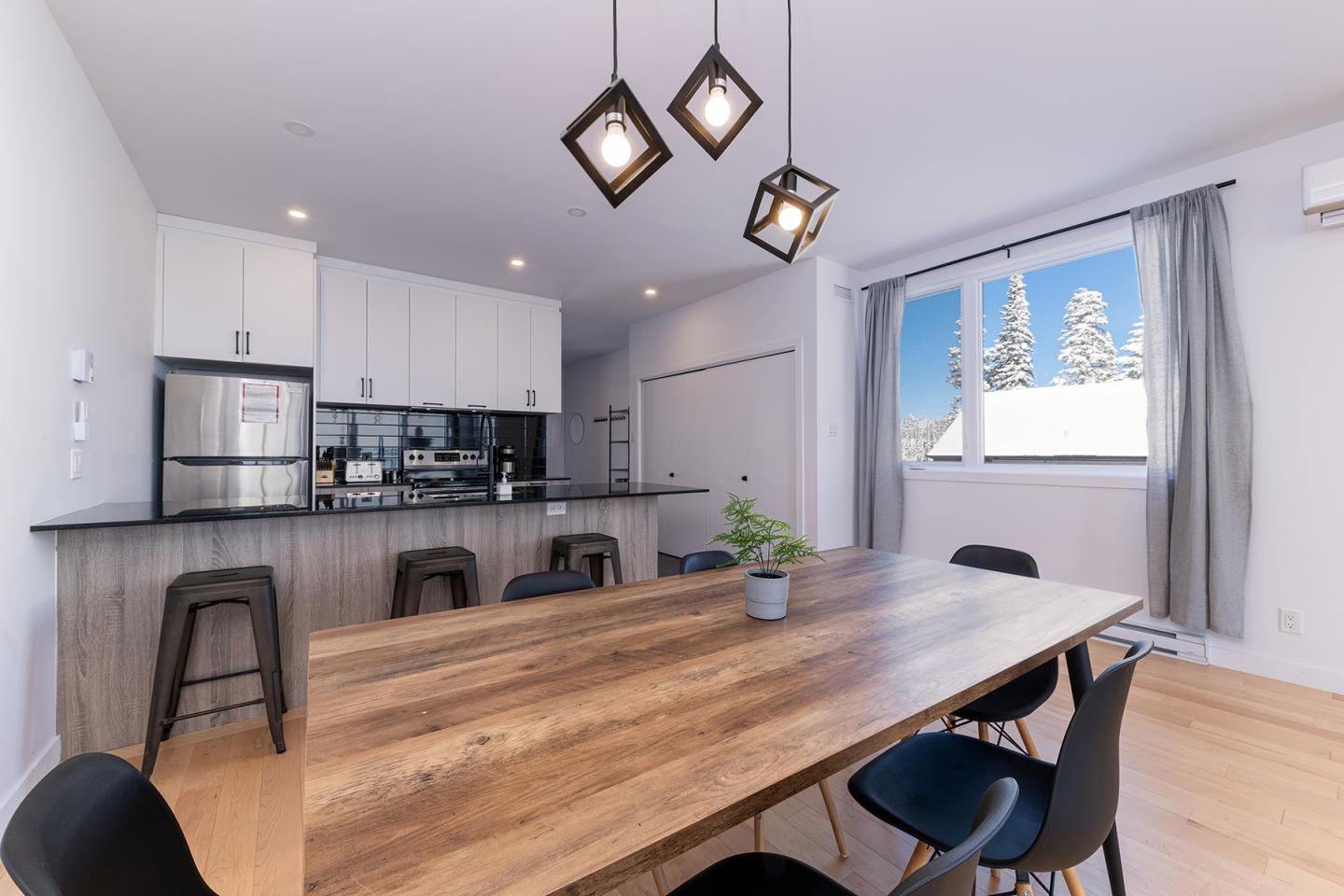 Cuisine moderne avec table en bois, chaises noires, et fenêtre ensoleillée.