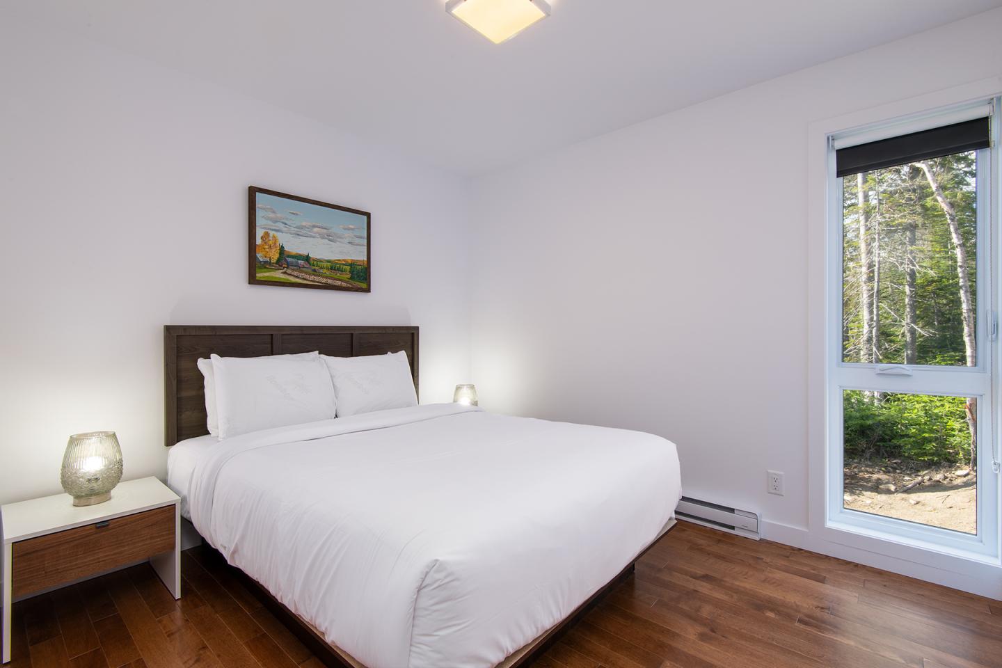 Chambre lumineuse avec lit double, murs blancs et fenêtre montrant un jardin.
