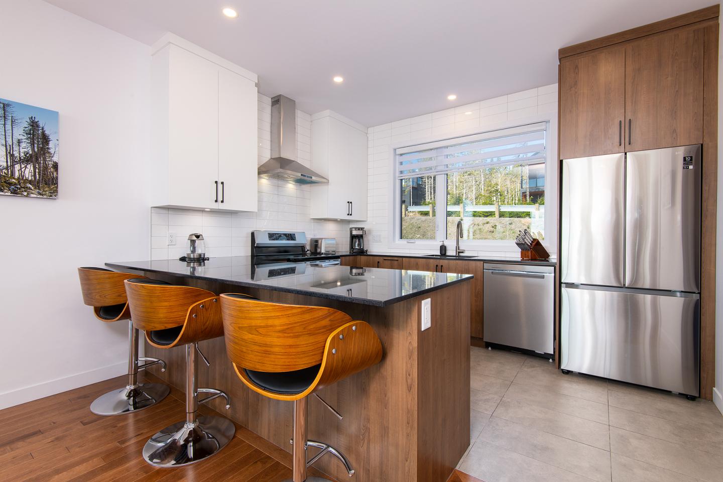 Cuisine moderne avec îlot central, tabourets en bois et appareils en acier inoxydable.