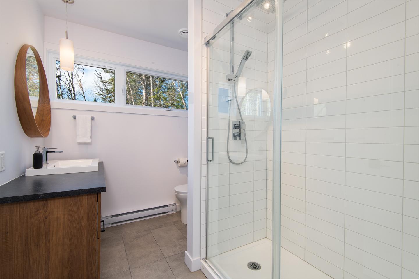 Salle de bain moderne avec douche vitrée, lavabo et grand miroir rond.