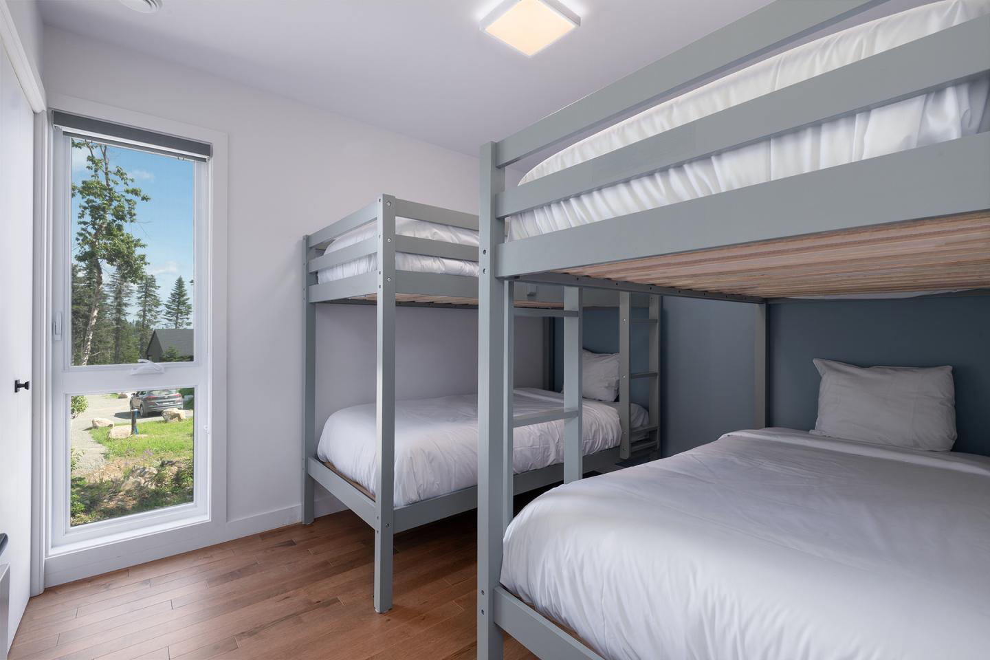 Chambre lumineuse avec deux lits superposés et vue sur jardin.