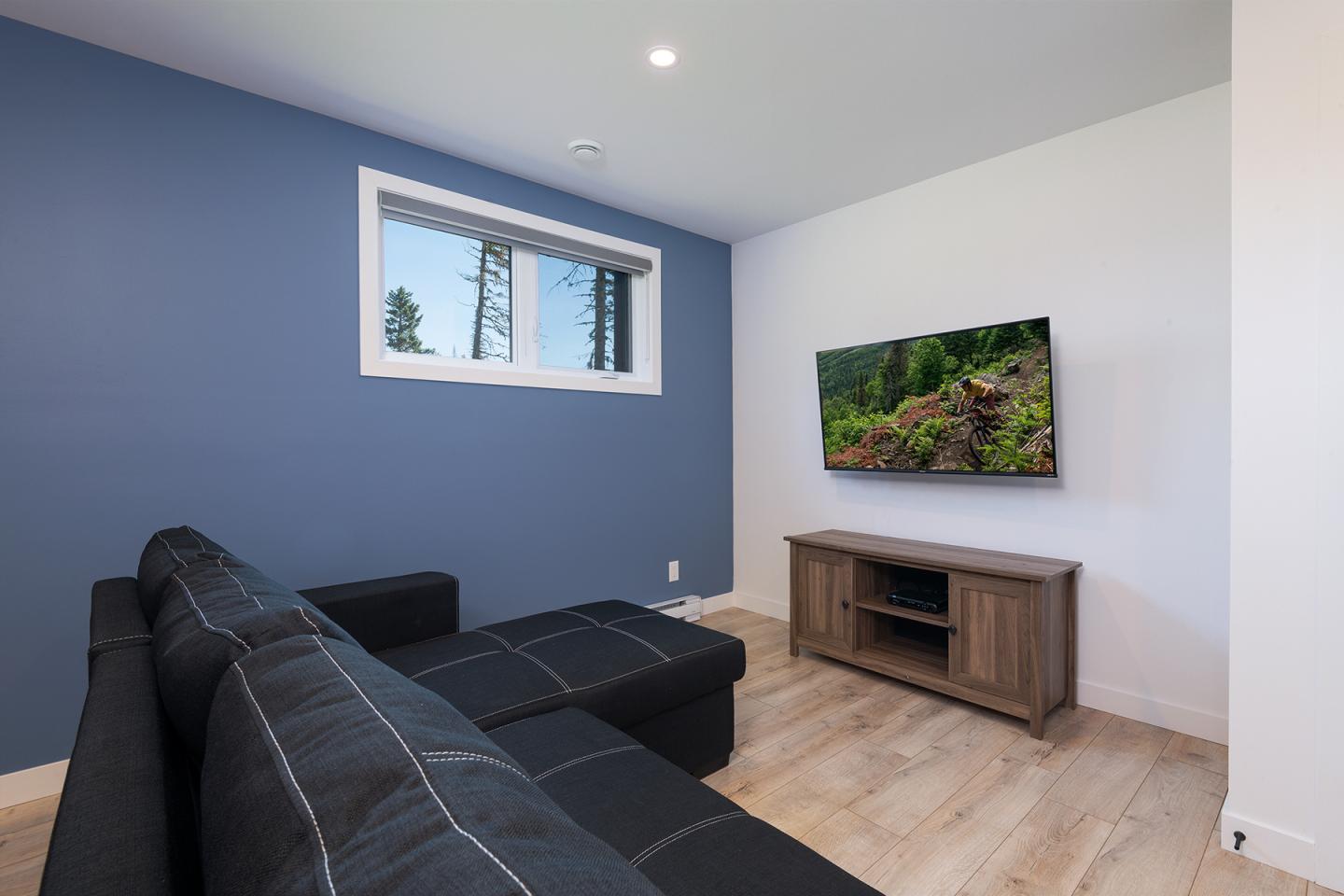 Salon moderne avec canapé noir, mur bleu, et TV murale.