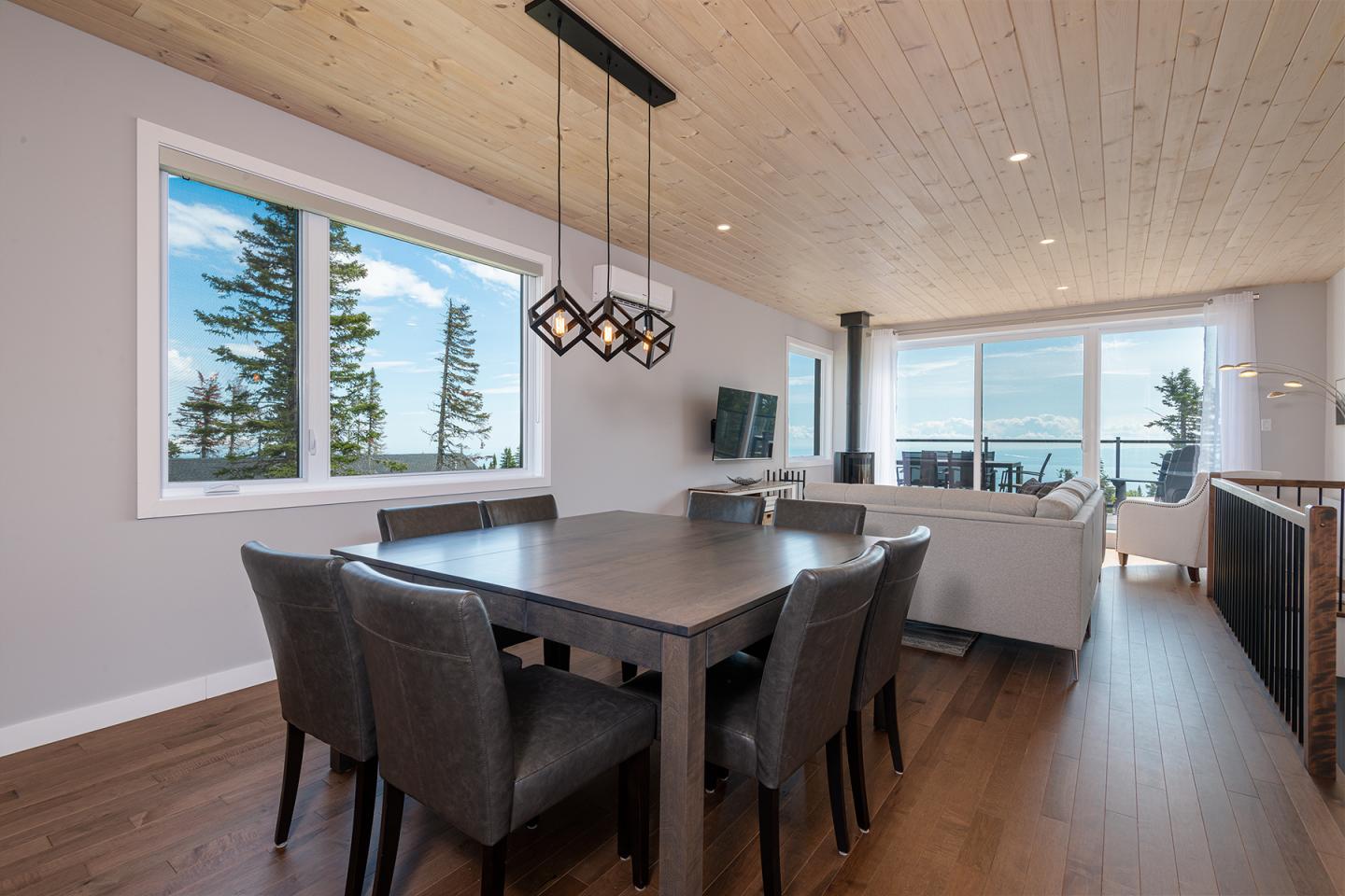 Salle à manger moderne avec vue sur un salon lumineux et fenêtres donnant sur des arbres et la mer.
