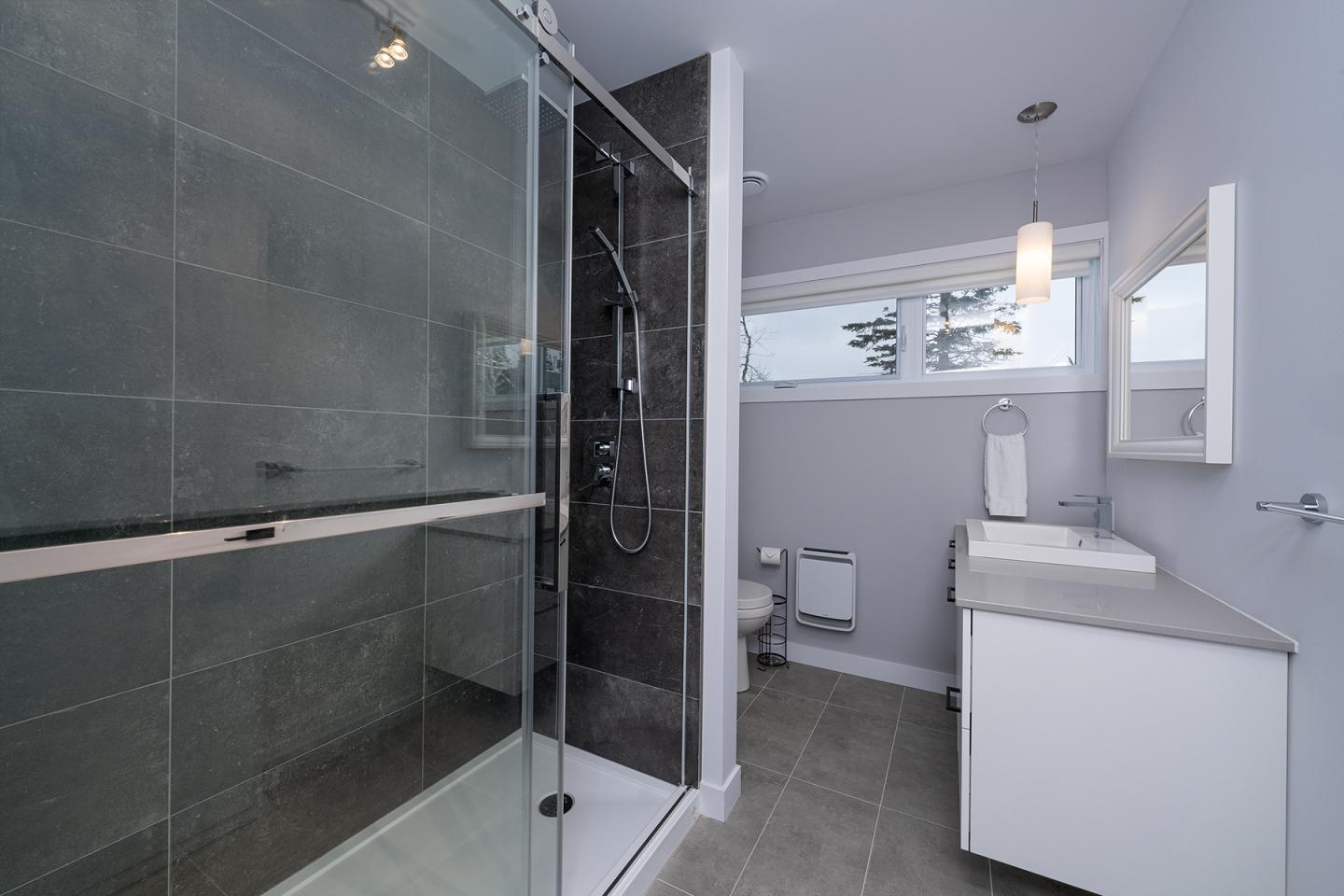 Salle de bain moderne avec douche vitrée et lavabo blanc.