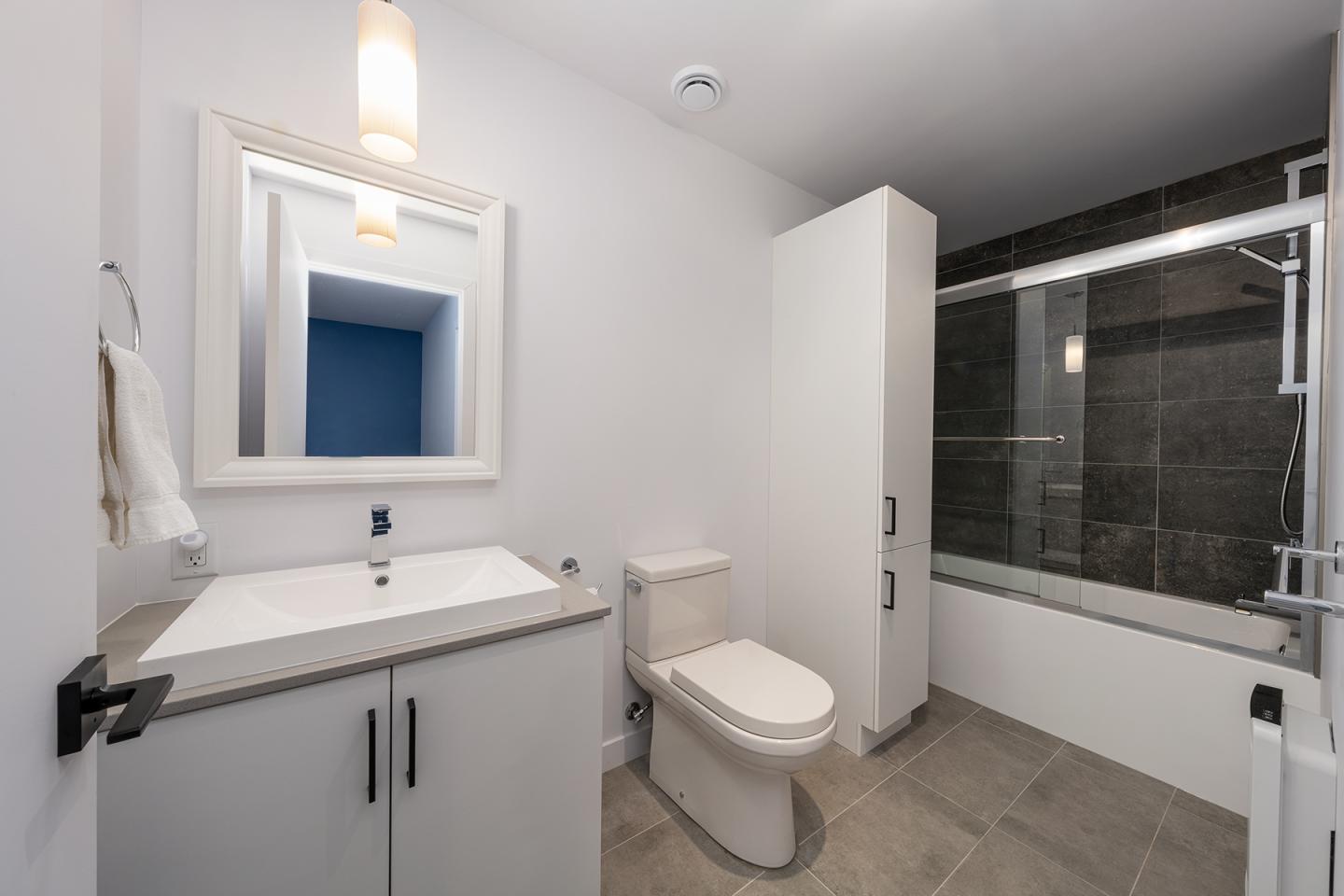 Salle de bains moderne avec vasque, toilette et baignoire, murs blancs et sol gris.