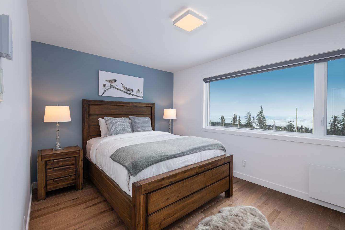 Chambre moderne avec lit en bois, vue sur des arbres par la fenêtre.