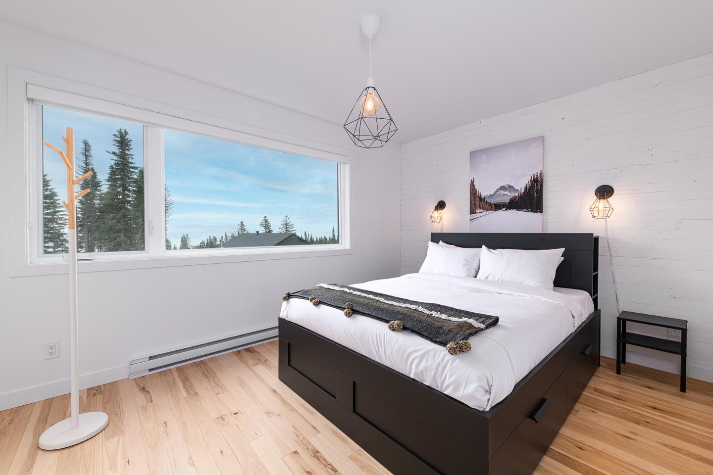Chambre lumineuse avec lit double, mur blanc, et fenêtre vue forêt.