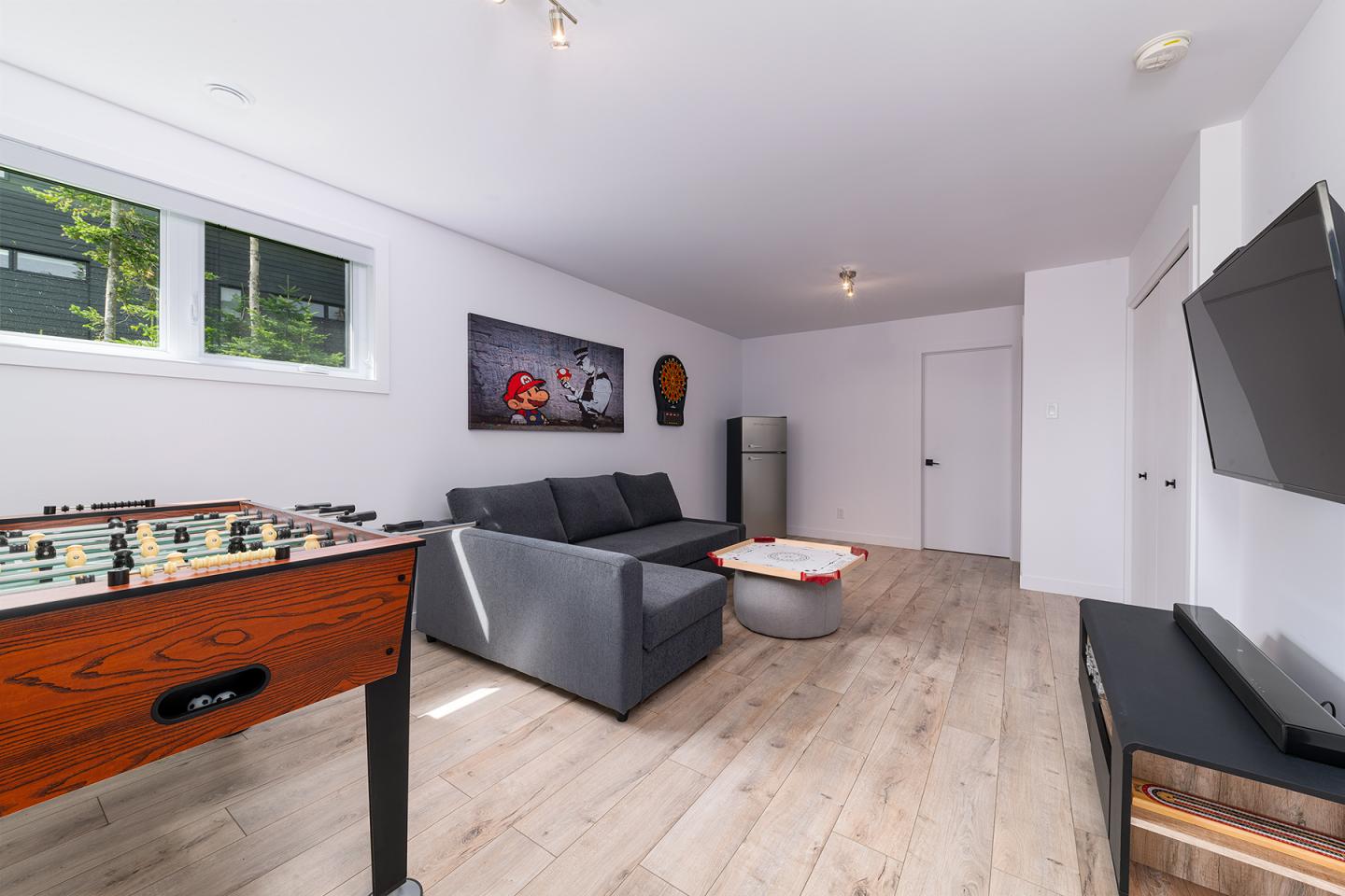 Salle de jeu moderne avec baby-foot, canapé gris et téléviseur mural.