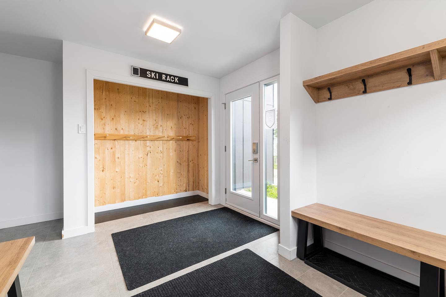 Entrée moderne avec bancs en bois, crochets et porte vitrées.