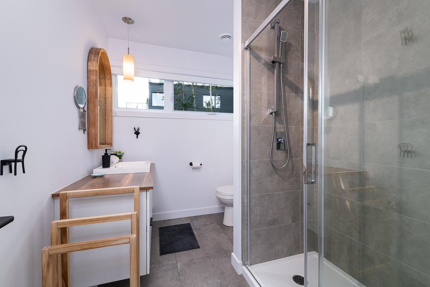 Salle de bain moderne, cabine de douche en verre, lavabo en bois, murs blancs.