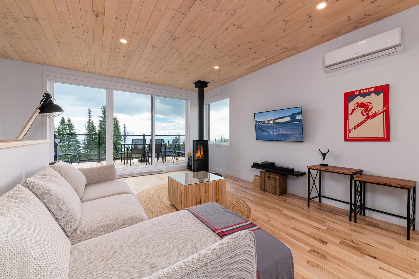 Salon moderne avec canapé beige, cheminée, grandes fenêtres et vue sur l'extérieur.