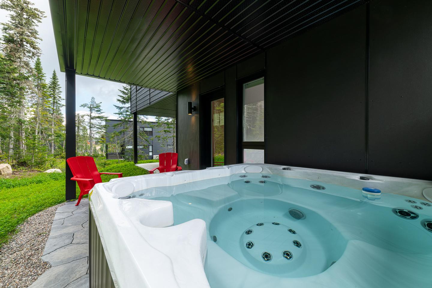 Spa extérieur avec chaises rouges, entouré de verdure et de conifères.