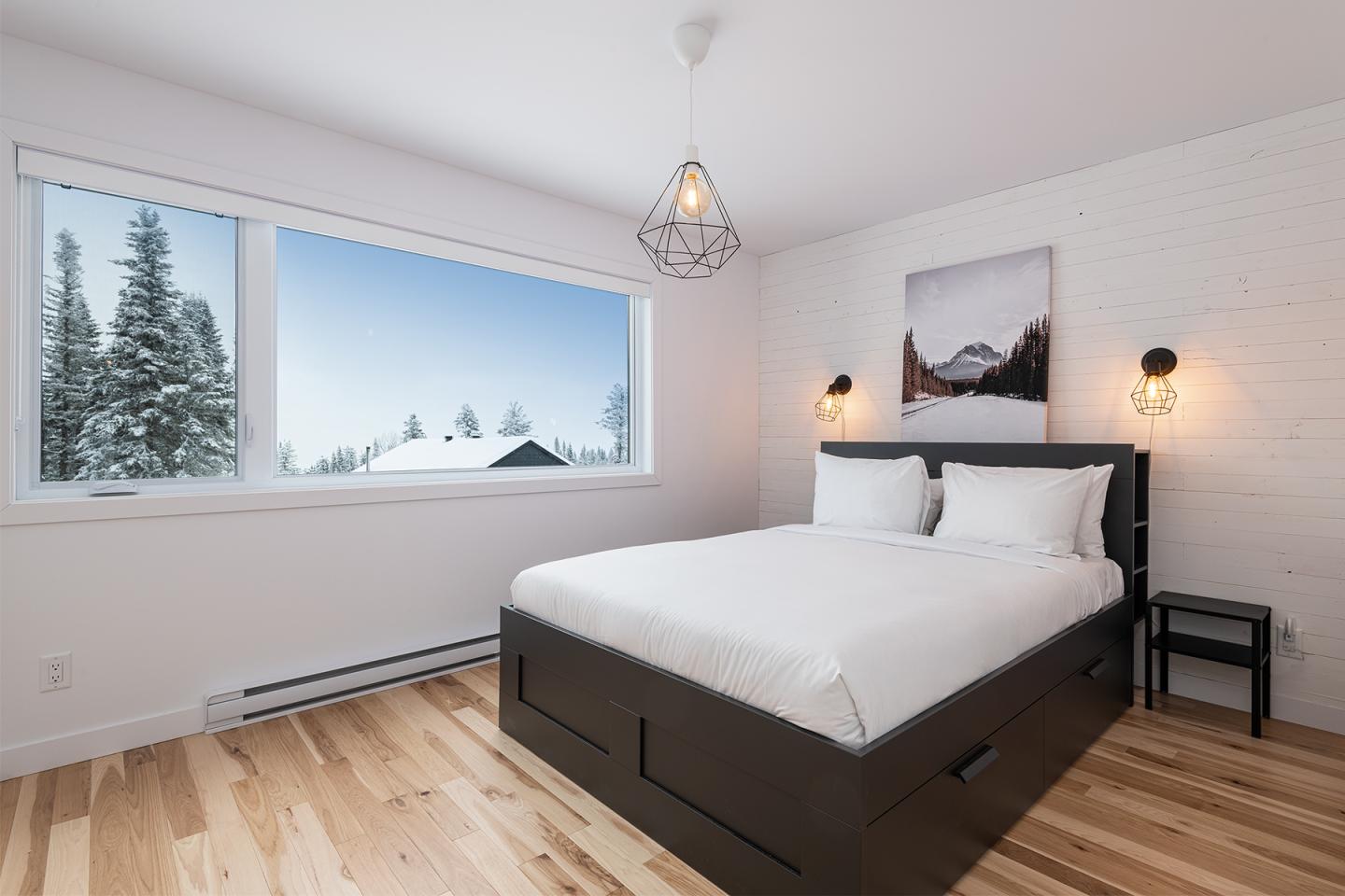 Chambre moderne avec lit double, parquet clair, vue sur neige par la fenêtre.