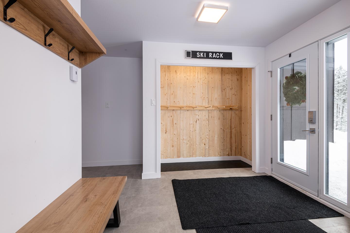 Hall d'entrée moderne avec banc en bois et porte en verre.