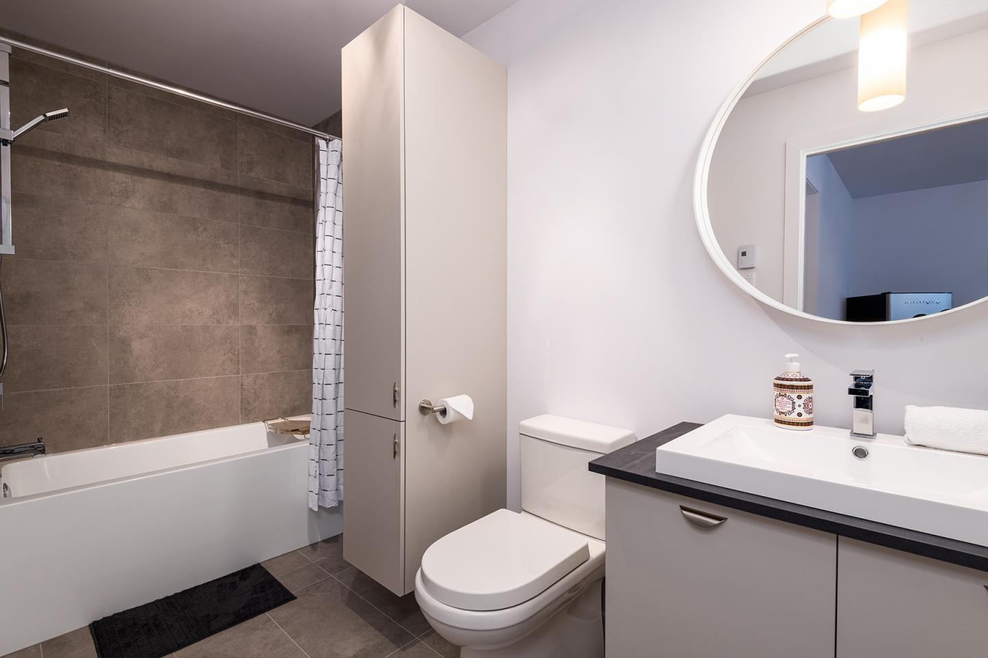 Salle de bain moderne avec baignoire, miroir rond et lavabo.