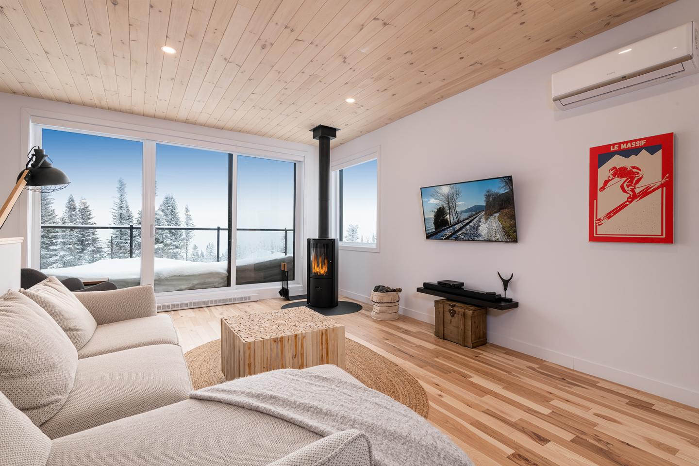 Salon moderne avec poêle à bois, canapé beige et vue sur paysage enneigé par la fenêtre.