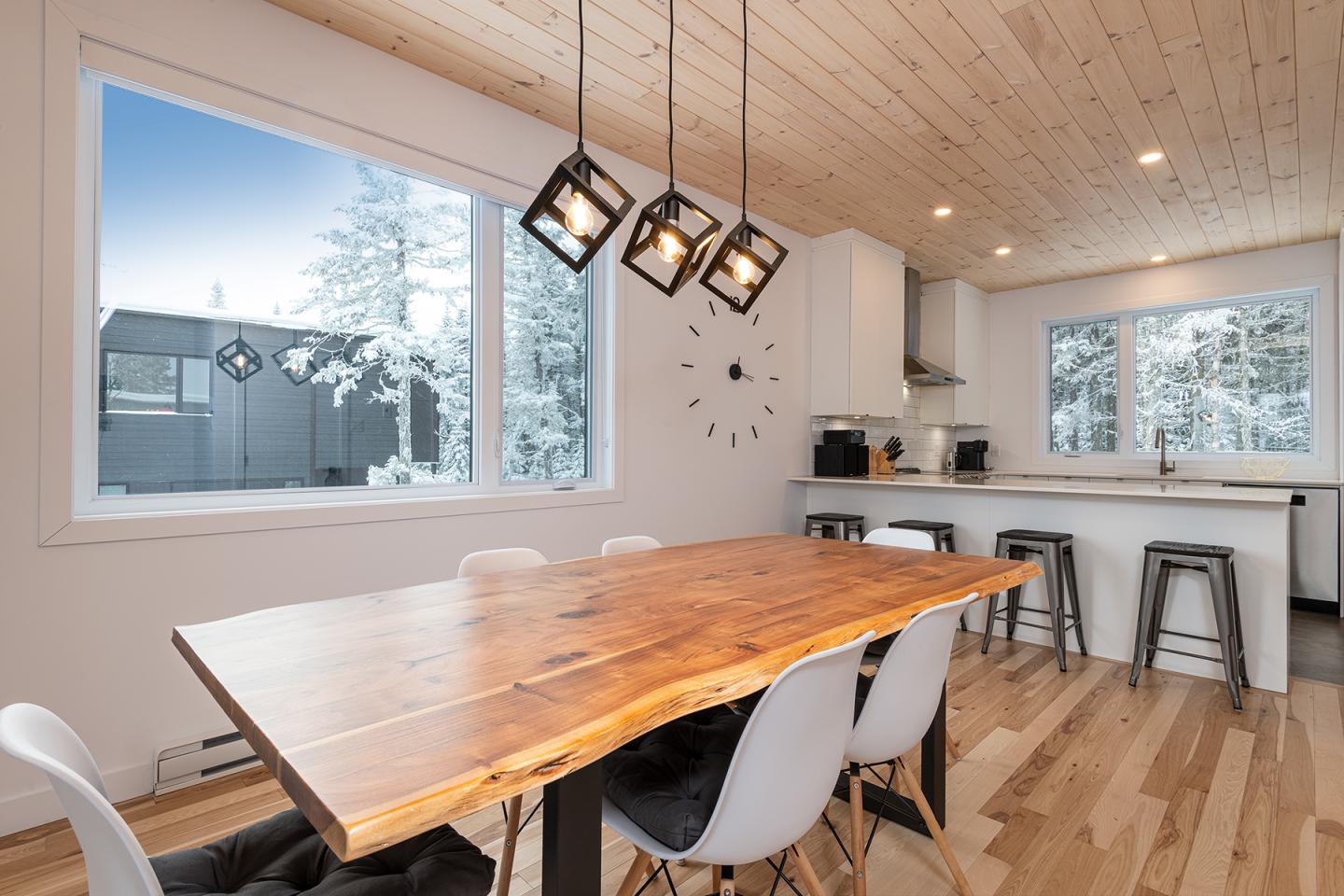 Salle à manger moderne avec table en bois, chaises blanches et grandes fenêtres.