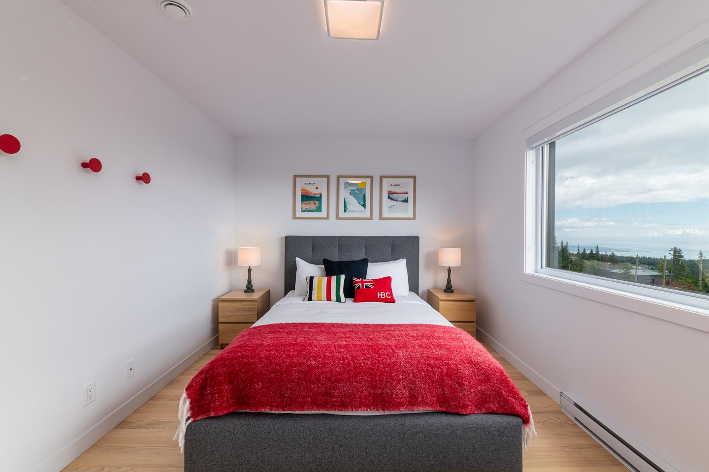 Chambre moderne avec lit, dessus-de-lit rouge, lampes de chevet et vue sur l'extérieur.