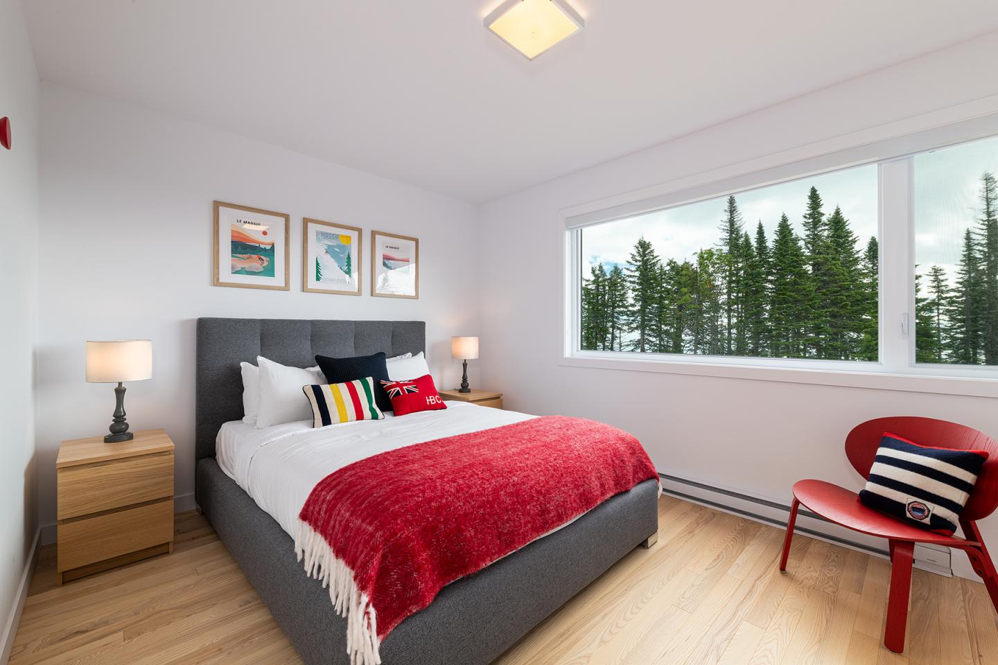 Chambre lumineuse avec lit double, plaid rouge et fenêtre donnant sur une forêt.