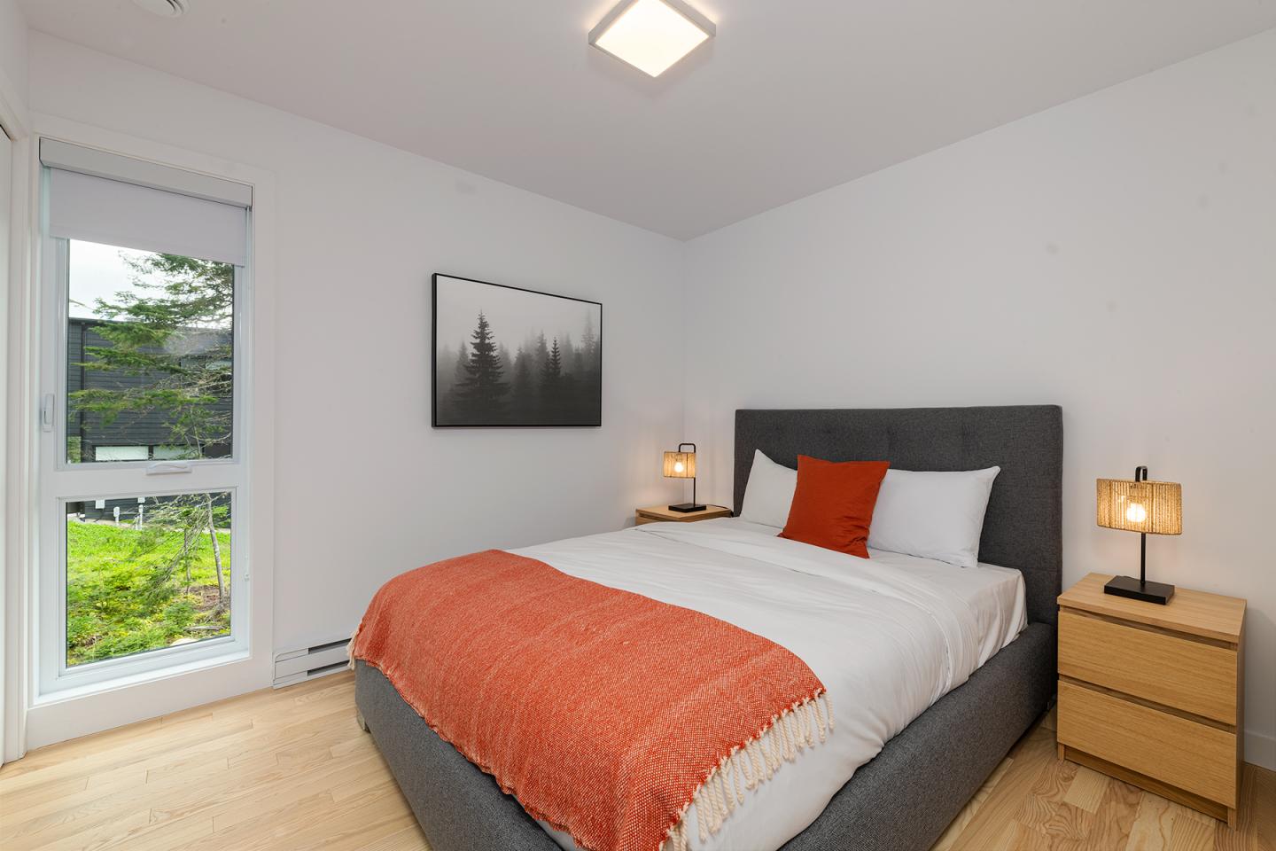 Chambre moderne avec lit double, couverture orange, et lampes de chevet.