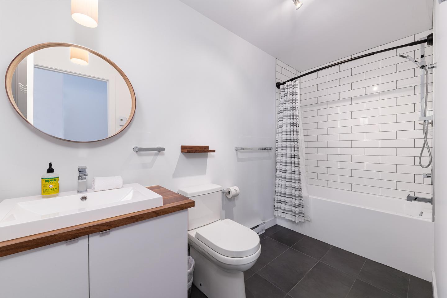 Salle de bain moderne avec baignoire, carrelage blanc et miroir rond.