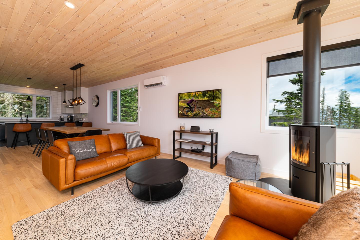 Salon moderne avec canapé en cuir orange, poêle noir et grandes fenêtres.