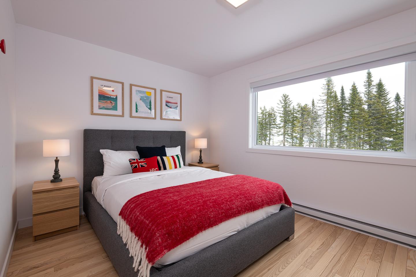 Chambre lumineuse avec lit double et couverture rouge, vue sur une forêt par la fenêtre.