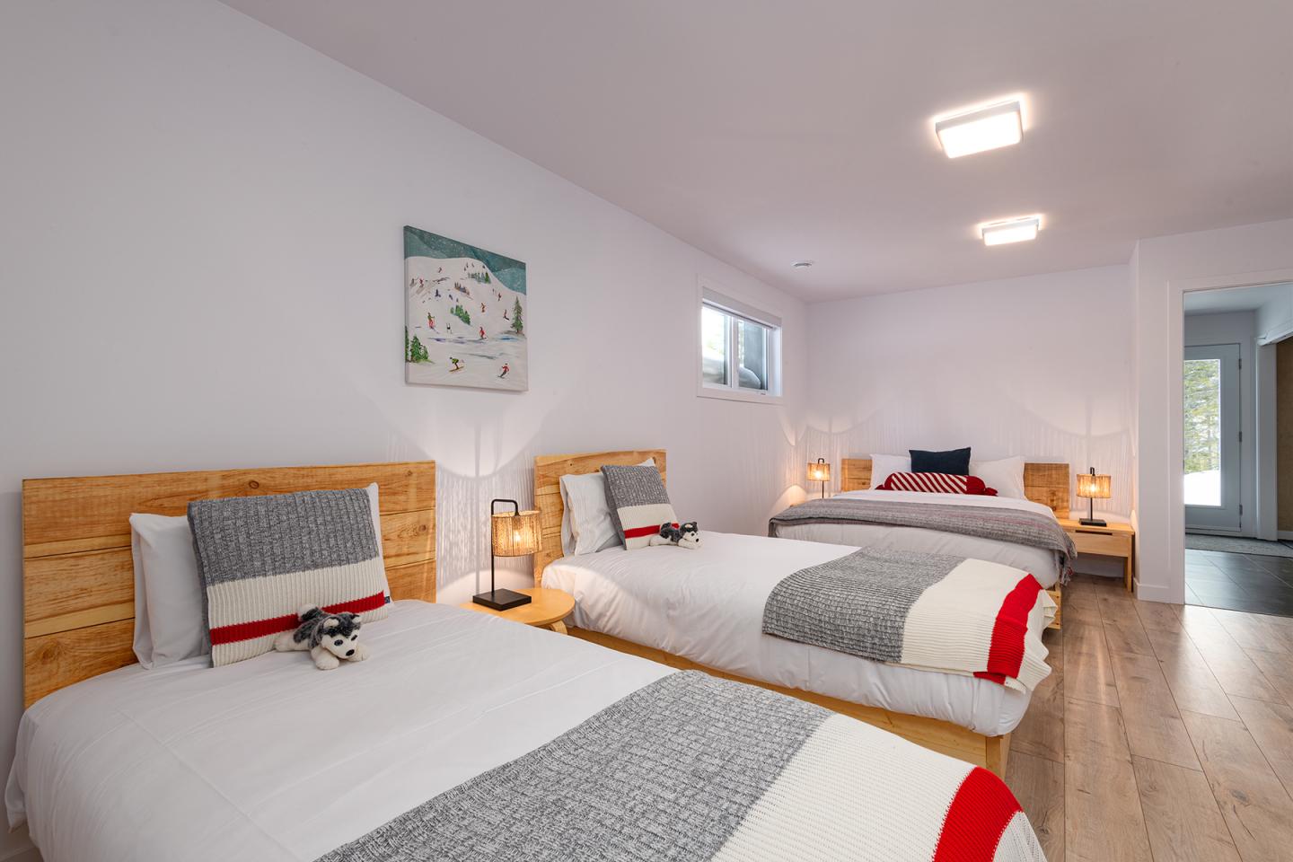 Chambre moderne avec trois lits, murs blancs et parquet clair.