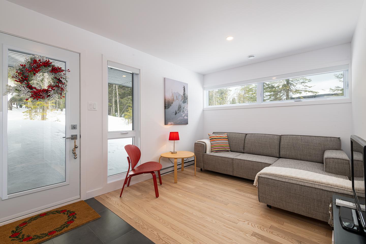 Salon moderne avec canapé gris, chaise rouge et lumière naturelle.
