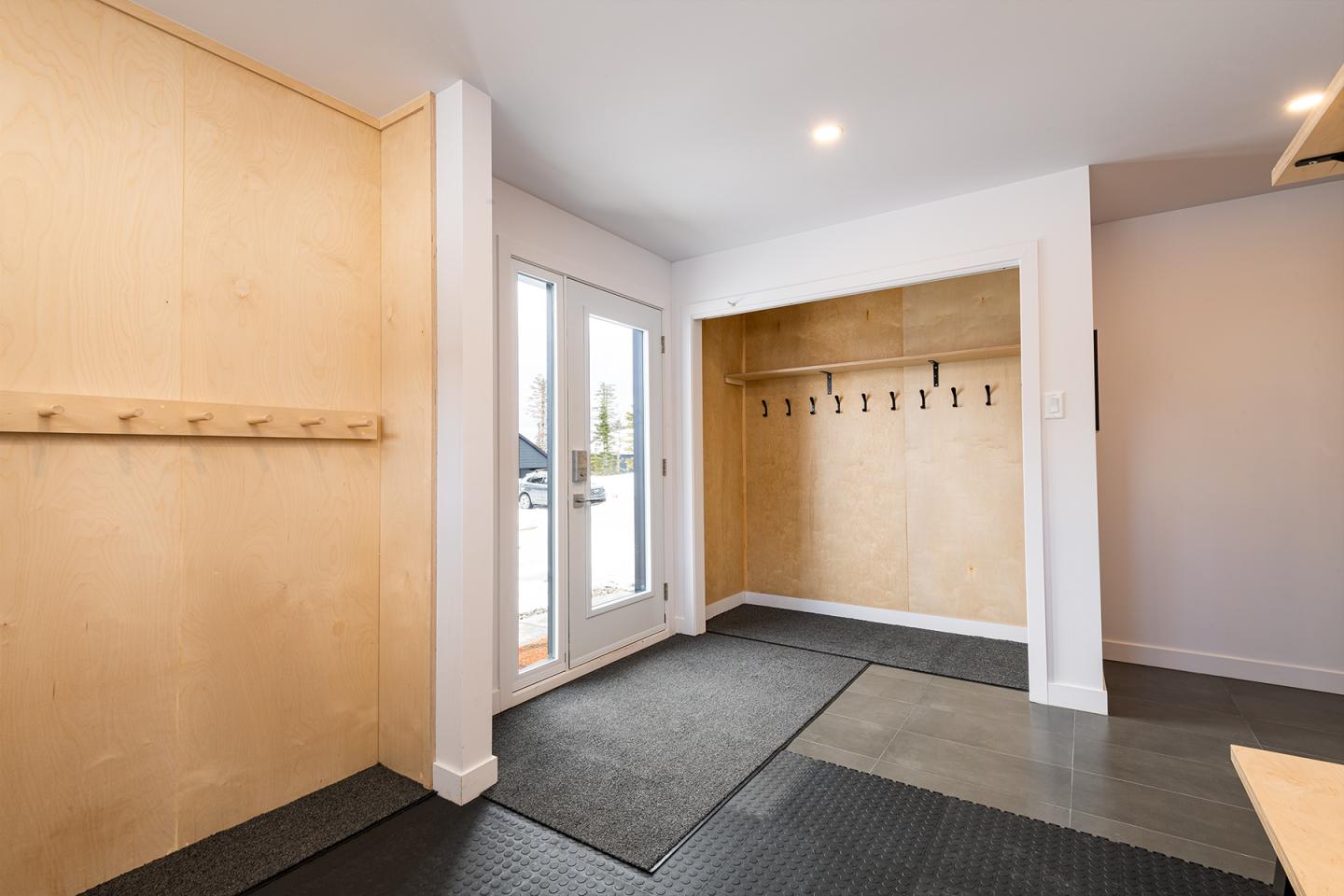 Entrée moderne avec murs en bois clair, porte vitrée, et tapis foncé.